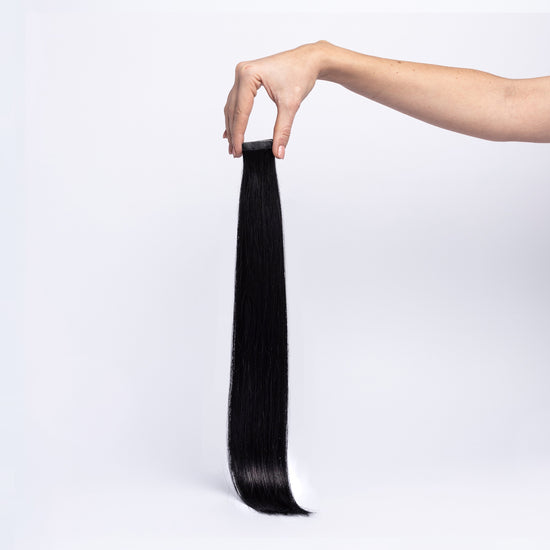 Einzelne chaarmant Classic Tape In Extension in Schwarz, 55 cm, freigestellt in der Hand gehalten
