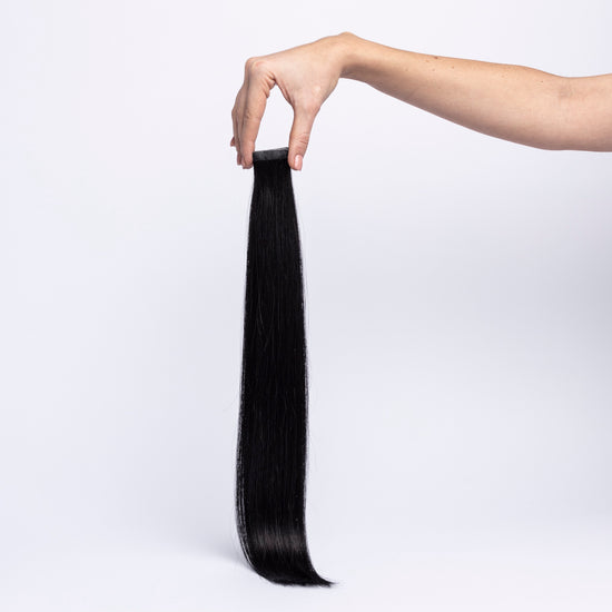 Einzelne chaarmant Classic Tape In Extension in Schwarz, 55 cm, freigestellt in der Hand gehalten
